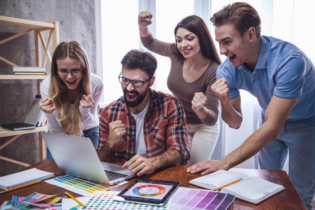A team celebrates a success in front of a laptop